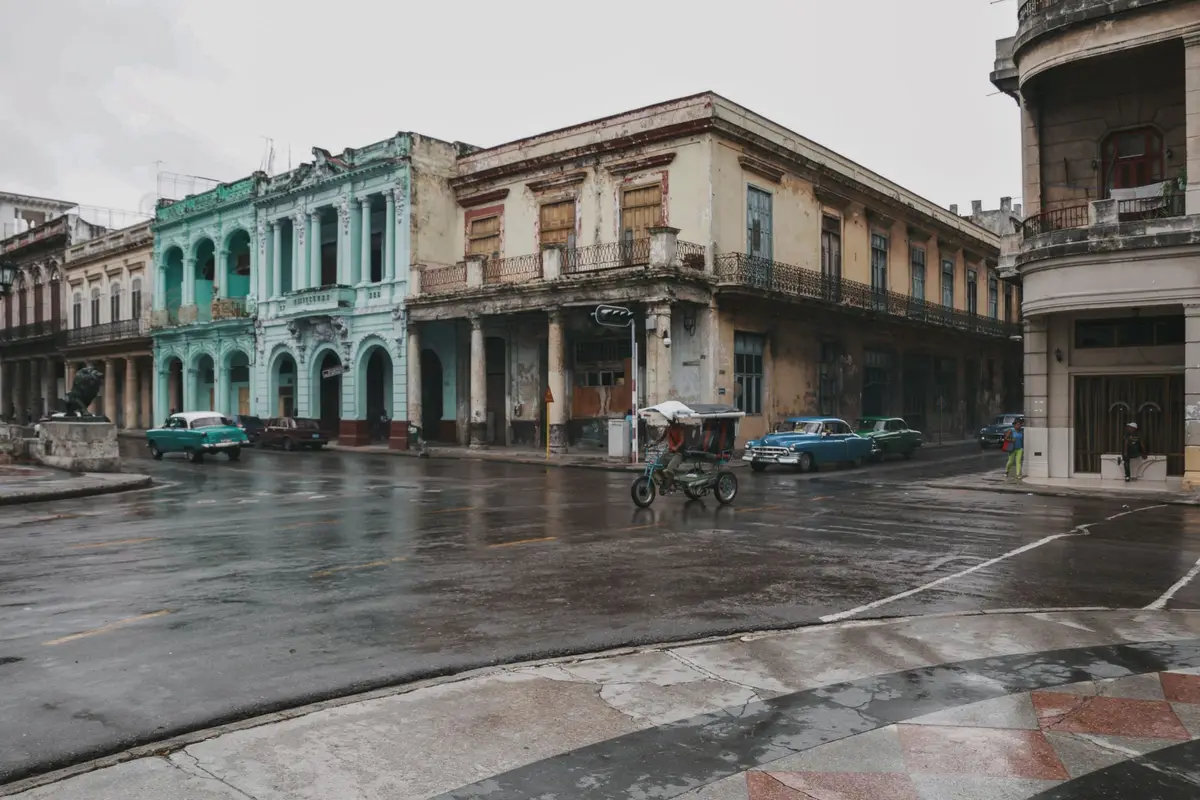 A rainy street in Havana with turquoise colonial facades and vintage cars