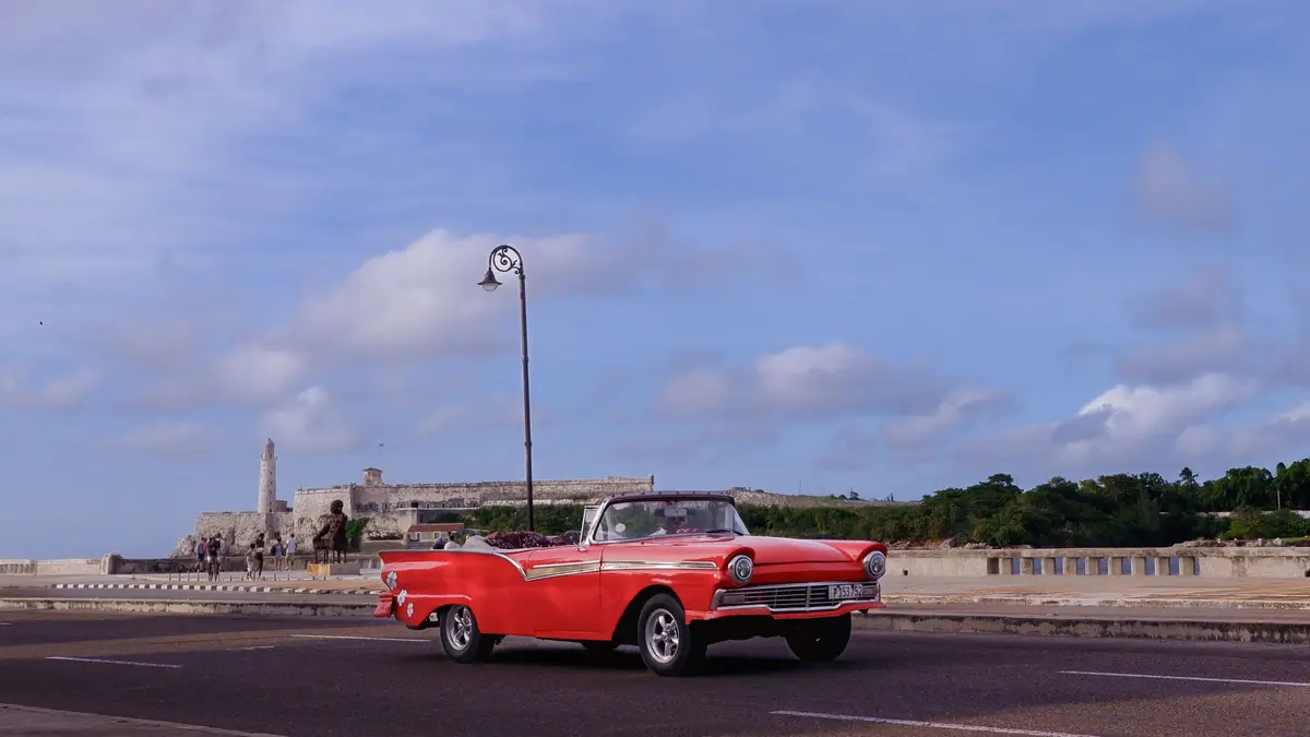 A red 1950s convertible on the Malecón with El Morro lighthouse behind